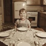 Bambino anni 50 soddisfatto guarda tavola apparecchiata senza bicchieri - metafora AI che dice ho finito troppo presto